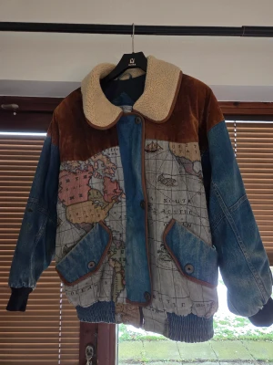 Vintage jeansjacka med världskarta - Unik vintage jeansjacka från Gallery med världskarta-print, bruna mockadetaljer och fluffig krage i teddy. Jackan har stora fickor med knappar, ribbade muddar och cool retro-vibe. Perfekt för dig som vill sticka ut med en statement piece.