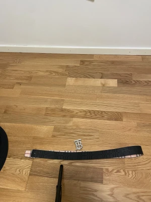  Burberry bälte - Säljer ett snyggt Burberry-bälte i skinn med klassiskt rutig design i beige, röd och svart. Bältet har en silverfärgad metallspänne med Burberrys ikoniska TB-logga. Perfekt för att lyfta din outfit med en lyxig touch.