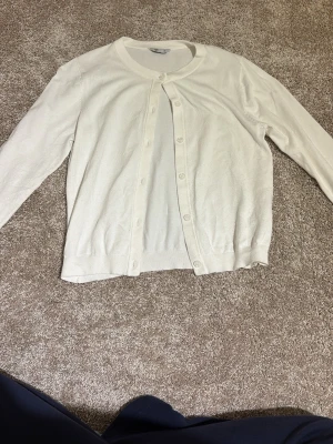 Vit kofta från Cubus i storlek XS - Säljer en stilren vit kofta från Cubus i storlek XS. Koftan har rund halsringning, långa ärmar och knäppning med matchande vita knappar framtill. Materialet känns mjukt och lätt, perfekt för lager-på-lager. Enkel och clean design som funkar till många outfits.