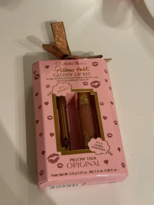 Charlotte Tilbury Pillow Talk Glossy Lip Kit - Säljer ett Pillow Talk Glossy Lip Kit från Charlotte Tilbury med en läppenna och ett läppglans i originalfärgen. Förpackningen är rosa med guldiga detaljer och en glittrig rosett. Perfekt för dig som gillar nude-rosa läppar med glansig finish.