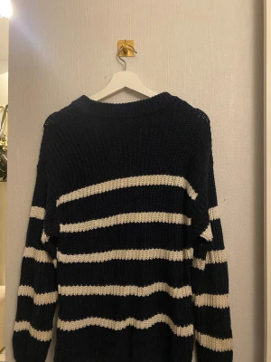 Randig stickad tröja i marinblått oversize - Säljer en grovstickad tröja med breda vita och marinblå ränder. Tröjan har rund hals och långa ärmar, perfekt för dig som gillar en chill och avslappnad stil. Materialet är mjukt och värmande, passar bra till jeans eller kjol.