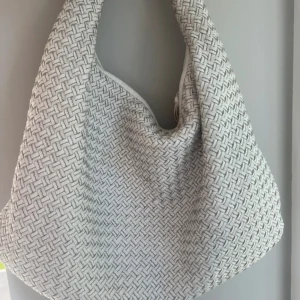 Vit axelväska från Bottega Veneta - Säljer en snygg axelväska från Bottega Veneta i vit skinn med ett unikt flätat mönster. Väskan har dragkedja och flera fack inuti med beige mockadetaljer. Perfekt storlek för att få plats med allt du behöver och riktigt stilren design. Köpt på collectors café i Köpenhamn för 10500kr och är endast använd en gång. Modellen heter ”Hobo” 