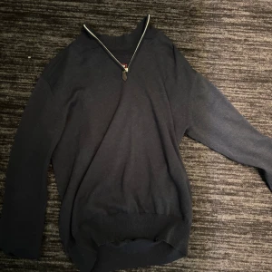 Mörkblå tröja med half zip - Mörkblå långärmad tröja med half zip-dragkedja vid halsen. Tröjan har ribbade muddar vid ärmslut och nederkant, vilket ger en snygg och enkel look. Perfekt för dig som gillar stilrena och bekväma plagg.