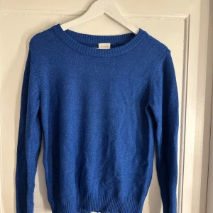 Blå stickad tröja från Vila - En klassisk blå stickad tröja från Vila i storlek XS. Tröjan har rund halsringning, ribbade muddar vid ärmslut och nederkant samt långärmad passform. Perfekt att styla med jeans eller kjol för en enkel och snygg look.