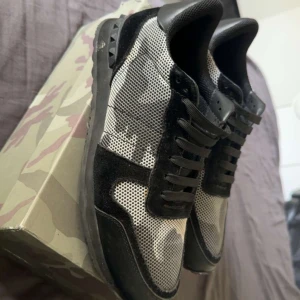 Valentino Rockrunners ( Med Kvitto ) - Säljer ett par Valentino Rockrunner sneakers i svart och grått med coolt kamouflagemönster. Skorna har svarta mockadetaljer, meshpaneler och klassiska nitar på sulan. Snygg och sportig siluett med snörning och rund tå. Kommer med originalkartong och röd dustbag.  Låda extra, snören och taggarna medföljer.  Skicka 9/10 använda ett fåtal gånger cirka 3 gånger.  Om ni vill se kvittot är det bara att skriva.