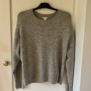 Grå stickad tröja från H&M - Mysig grå stickad tröja från H&M i storlek S. Tröjan har rund halsringning, ribbade muddar vid ärmslut och nederkant samt en loose passform. Perfekt för lager-på-lager under kyliga dagar.