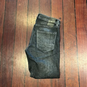 Svarta jeans från Jack & Jones - Snygga svarta jeans från Jack & Jones med klassisk femficksdesign och raka ben. Jeansen har en mörk tvätt med subtila slitningar och kontrastsömmar. Perfekta för dig som gillar en stilren och enkel look. Materialet är robust denim i bomull.