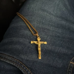 Guldfärgat korshalsband med Jesus - Säljer ett snyggt guldfärgat halsband med ett kors och Jesusfigur som hänge. Kedjan är klassisk och korshänget har fina detaljer. Perfekt för dig som vill ha ett statement-smycke med religiös touch.