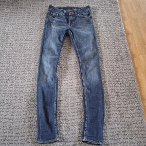 Blå skinny jeans från Tiger of Sweden - Snygga blå jeans från Tiger of Sweden med klassisk femficksdesign och smal passform. Jeansen har kontrastsömmar och en mörk tvätt med lätt slitning. Perfekta för dig som gillar en stilren och modern look.