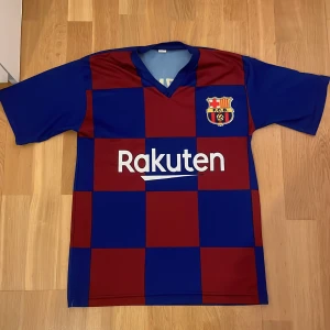 FC Barcelona Griezmann 17 matchtröja S - Säljer en officiell FC Barcelona matchtröja med Griezmann 17-tryck. Tröjan har klassiskt rutigt mönster i blått och rött, korta ärmar och klubbmärke på bröstet. Materialet är lätt och andas, perfekt för fotboll eller att bära på läktaren.