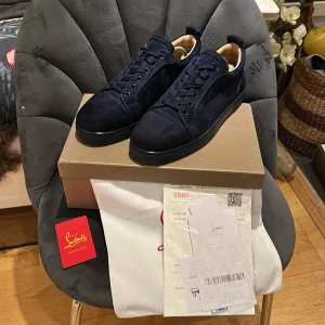 Loubitin skor - Snygga mörkblå sneakers från Christian Louboutin i lyxig mocka med klassisk snörning och ikoniska röda sulor. Skorna har rund tå och diskret broderad logga på hälen. Perfekta för dig som vill sticka ut med exklusiv stil.