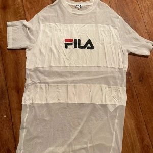 Vit meshklänning från FILA - Vit transparent meshklänning från FILA med korta ärmar och stort logotryck framtill. Oversized passform och sportig vibe, perfekt att styla över andra plagg för en cool look.