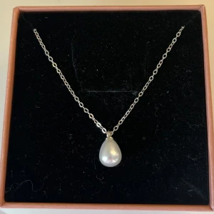 Silverhalsband med droppformad pärla - Elegant halsband i silver med en droppformad vit pärla som hänge. Kedjan är tunn och stilren, perfekt för att ge en klassisk touch till din look. Passar dig som gillar tidlösa smycken med en enkel men lyxig känsla. I rostfritt stål och handgjort 
