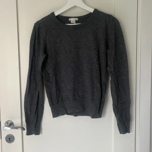 Mörkgrå basic tröja från H&M - En enkel och stilren mörkgrå tröja från H&M Basic. Tröjan har rund halsringning, långa ärmar och ribbade muddar vid hals och ärmar.
