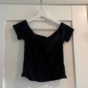 Svart ribbad topp från H&M Basic - Svart ribbad topp från H&M Basic med korta ärmar och snygg v-ringning. Modellen är figurnära och har en enkel, stilren design som passar till många olika looks. Perfekt att matcha med jeans eller kjol för en trendig outfit.