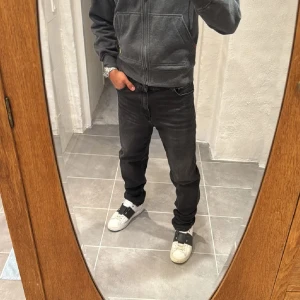 Svarta Replay jeans straight fit - Säljer ett par svarta jeans från Replay med klassisk femficksdesign och raka ben. Jeansen har en mörk tvätt och subtila sömmar, perfekt för en clean och stilren look. Materialet är mjukt och stretchigt jeans för extra komfort.