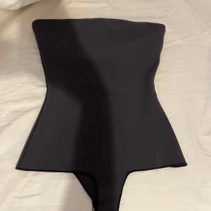 Svart bandeau baddräkt från Zara - Supersnygg svart bandeau baddräkt från Zara med stilren och minimalistisk design. Baddräkten har en axelbandslös form och knäppning i grenen för extra smidighet. Perfekt för dig som gillar en clean och modern look på stranden.