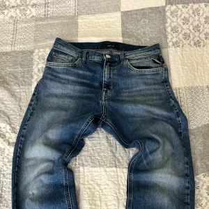 Blå Replay jeans med raka ben - Snygga blå jeans från Replay med klassisk femficksdesign och raka ben. Jeansen har en cool tvätt med slitningar och tydliga sömmar, samt Replay-logga på bakfickan och läderpatch i midjan. Perfekta för dig som gillar en avslappnad men stilren look.