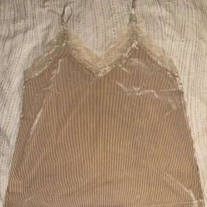 Champagnefärgad linnetopp med spets - Säljer en innetopp med tunna axelband. Tröjan är aldrig använd bara testad på en gång. Tyvärr är inte etiketten kvar.