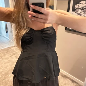 Svart topp - Säljer en svart topp med tunna axelband. Toppen har en söt rynkad detalj vid bysten och en figurnära passform upptill som sedan faller ut i en volang nertill. Köpt på Vinted men ursprungligen från Zara 