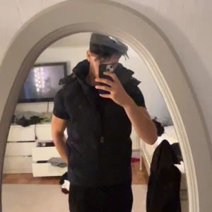 Svart dunväst från Polo Ralph Lauren - Säljer en svart dunväst från Polo Ralph Lauren med avtagbar huva och klassisk broderad logga på bröstet. Västen har två sidofickor med dragkedja och en snygg röd detalj på insidan. Perfekt för lager-på-lager och chill stil. Pris är ej hugget i sten så skriv vid intresse