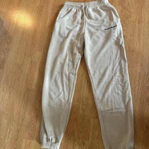 Beiga mjukisbyxor Supply & Demand XXS - Beiga mjukisbyxor från Supply & Demand med resår och snörning i midjan. Byxorna har en avslappnad passform och logga tryckt på ena låret. Perfekta för chill dagar och har elastiska muddar vid bensluten.