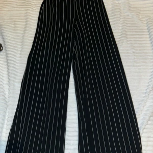 Svarta vida byxor med vita ränder - Snygga svarta byxor med vita vertikala ränder i modellen Jenna trousers. Byxorna har en vid passform och hög midja.