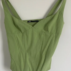 Grön korsettopp från Zara XS - Snygg ljusgrön korsettopp från Zara i storlek XS. Toppen har breda axelband, markerade sömmar och en figurnära passform. Perfekt att styla med jeans eller kjol för en trendig look. Använd enbart en gång!