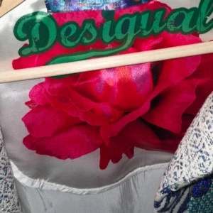 Desigual mönstrad kavaj i blå toner - Unik kavaj från Desigual med patchworkmönster i blått, turkost och beige. Jackan har långa ärmar, knappar framtill och insida med stor röd ros. Materialet är vävt och känns rejält, perfekt för dig som gillar statement-plagg och färg.