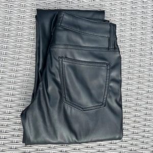 Svarta skinnbyxor från 157 Icon - Snygga svarta skinnbyxor från 157 Icon med klassisk femficksdesign och raka ben. Byxorna har normal passform och är tillverkade i ett glansigt skinnmaterial som ger en cool look. Perfekta för dig som vill sticka ut med en edgy stil.