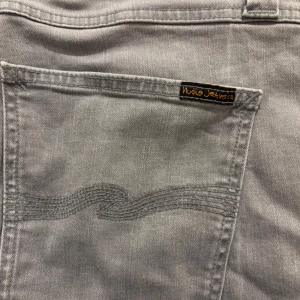 Ljusgrå jeans från Nudie Jeans - Säljer ett par ljusgrå jeans från Nudie Jeans med klassisk femficksdesign och snygga broderade bakfickor. Jeansen har raka ben och är tillverkade i mjuk bomullsdenim. Perfekta för dig som gillar stilrena och bekväma jeans. Modell lean Dean och är mer eller mindre i perfekt skick då de knappt kommit till användning 