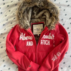 Röd hoodiejacka Abercrombie & Fitch S - !!!! KAN ÄVEN BYTA MOT EN LIKNANDE I BLÅA FRÅN HOLLISTER ELLER ABERCROMBIE !!!!  Röd hoodiejacka från Abercrombie & Fitch med broderad logga och text på bröstet och ärmen. Jackan har dragkedja, ribbade muddar och en mysig huva fodrad med fuskpäls. Perfekt för dig som gillar streetstyle och vill ha något varmt och snyggt. Storlek S men passar mer som XS. 
