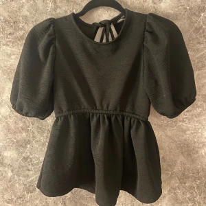 Svart blus  - Supersnygg svart topp/blus från Gina Tricot med puffiga korta ärmar och volang nertill. Tillverkad i ett lätt strukturerat tyg som känns bekvämt och luftigt. Helt ny med prislapp, aldrig använd, säljer då den aldrig kommit till användning. Pris kan diskuteras!💕