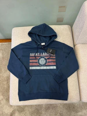 Saint Laurent hoodie - ⚠️Prislappen sitter ej på längre⚠️ Mörkblå hoodie från Saint Laurent i exklusiv och stilren design. Klassisk modell med huva, känguruficka och tryck framtill. Tillverkad i högkvalitativt material med mycket bra passform och komfort. En eftertraktad hoodie från ett lyxmärke som håller över tid.  📦 Skickas inom 24 timmar 🚭🐾 Från rök- och djurfritt hem 💰 Snabb affär = bättre pris, hör av dig!