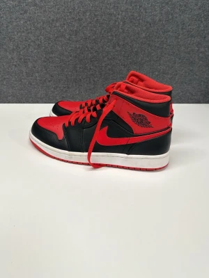 Nike Air Jordan 1 svart/röd sneakers - Säljer ett par Nike Air Jordan 1 sneakers i svart och rött med klassisk high-top siluett. Skorna har röd yttersula, svarta och röda paneler i skinn samt röda snören och detaljer. Ikonisk Air Jordan-logga på sidan och perforerad tåbox för extra stil. Helt oanvända. Skriv angående frågor!