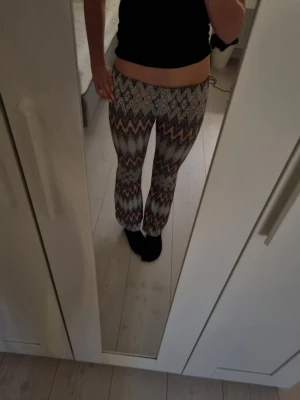 Mönstrade bootcut byxor i stretch - Säljer ett par trendiga snygga bootcut byxor med färgglatt zigzag-mönster i svart, ljusblått och orange. Byxorna har låg midja och är väldigt elastiska
