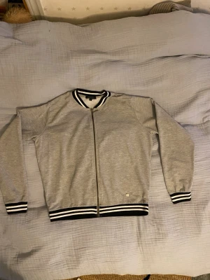 Grå bomberjacka med svarta detaljer - Snygg grå bomberjacka från tindra. Passar olika stilar beroende på vad den stylars med. Står storlek M men jag har xs och passar även S. skriv om ni undrar om något 💕