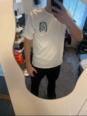 Vit Casablanca t-shirt med tryck - Säljer en vit t-shirt från Casablanca i storlek M. T-shirten har tryck både fram och bak med motiv av ett fönster och gröna blad samt texten 'Avenida Casablanca'. Tillverkad i 100% polyester och har klassisk passform med korta ärmar.