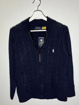 Marinblå kabelstickad kofta Polo Ralph Lauren - Kabelstickad marinblå kofta från Polo Ralph Lauren i storlek S. Rekommenderad läng där 165-175cm lång.