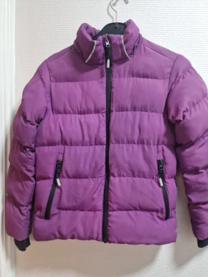 Lila pufferjacka från McKinley - Säljer en lila pufferjacka från McKinley i storlek 134/140. Jackan har hög krage, svarta dragkedjor och två fickor framtill. Perfekt för kalla dagar och riktigt skön att bära. Klassisk quiltad look och passar till det mesta.
