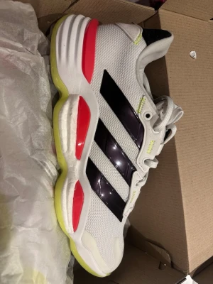 Snygga skor i storlek 42 3/4 - Snygga Adidas sneakers i vitt mesh med svarta och neonfärgade detaljer som aldrig är använda. Låg modell med snörning och sportig vibe, perfekt för dig som spelar ex. handboll, tennis, innebandy eller basket. I storlek 42 3/4. Ny kostar 1800kr 