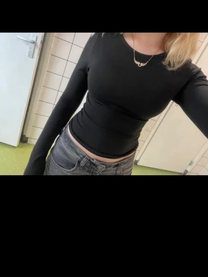 Svart croppad långärmad topp - Säljer en svart, croppad långärmad topp med tight passform. Toppen har rund halsringning och är gjord i ett stretchigt material som sitter snyggt på kroppen. Perfekt att styla med höga jeans eller kjol.