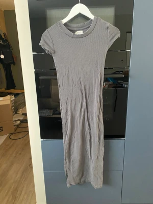 Grå ribbad långklänning Zalando - Säljer en enkel och stilren grå långklänning från Zalando Essentials. Klänningen är ribbad, har korta ärmar och rund halsringning. Perfekt för dig som gillar en clean och avslappnad look. Materialet känns mjukt och stretchigt.