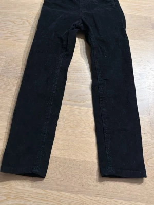 Svarta manchesterbyxor från H&M - Säljer ett par svarta manchesterbyxor från H&M med elastisk midja. Byxorna har en rak passform och är tillverkade i mjuk manchester som ger en skön känsla. Perfekta för dig som gillar klassisk stil med en twist.