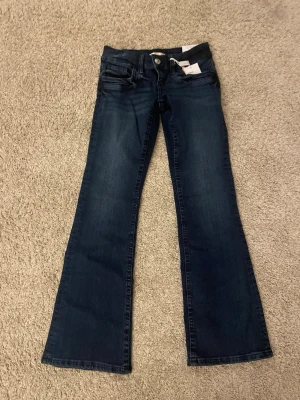 Mörkblå bootcut jeans från Gina tricot  - Säljer ett par mörkblå bootcut jeans från Gina tricoti storlek 152. Jeansen har låg midja, klassiska fem fickor och snyggt utsvängda ben. Materialet är jeans i bomullsmix och färgen är djup blå. Perfekta för dig som gillar retrovibbar och vill ha en bekväm passform.