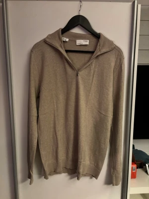 Beige half zip tröja Selected Homme - Säljer en beige långärmad tröja från Selected Homme med half zip och hög krage. Tröjan har en clean look och är tillverkad i mjuk bomull, perfekt för lager på lager under höst och vår. Passformen är normal och färgen är lättmatchad till det mesta.