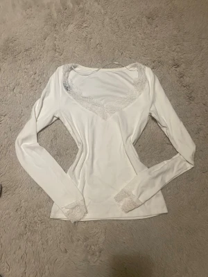 Vit långärmad spetsblus från Amisu - Supersöt vit långärmad blus från Amisu med v-ringning och spetsdetaljer vid halsringning och ärmslut. Tunn och mjuk i materialet, perfekt för lager på lager eller som den är. Enkel men ändå elegant look.