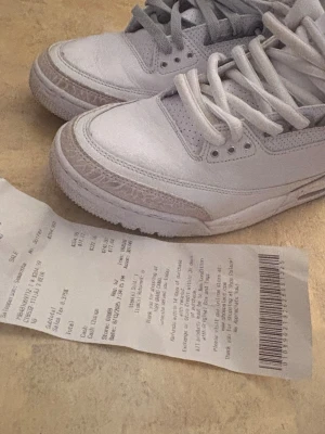 Nike Air Jordan 3 Retro pure money  - Nike Air Jordan 3 Retro pure money i vit och ljusgrå färg med klassisk Jumpman-logga på hälen. Skorna har snörning, rund tå och detaljer i skinn samt mönstrad grå panel vid tån och hälen. Snygg och tidlös modell som passar till streetwear och sneakersamlingen.