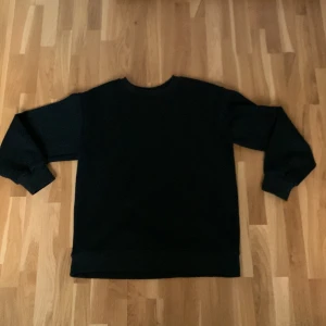 Svart sweatshirt från Stone Island - Svart sweatshirt från Stone Island med klassisk rund hals och ribbade muddar. Tröjan har den ikoniska Stone Island-loggan som kan fästas på ärmen. Tillverkad i mjuk bomull för en skön och avslappnad stil.