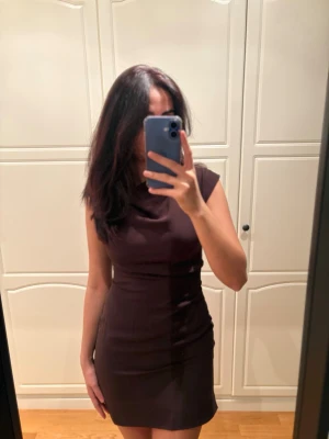 Mörkbrun kort klänning från MNG - Säljer en mörkbrun, figurnära kort klänning från MNG i storlek XS. Klänningen är ärmlös med hög halsringning och har en diskret dragkedja i ryggen. Den har används endast en gång. 